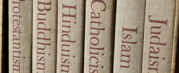 book spines that read respectively, protestantism, buddhism, hinduism, catholicism, islam, and judaism